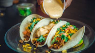 Golden tacos filled with juicy meat and drizzled with creamy sauce, served with a side of fries.