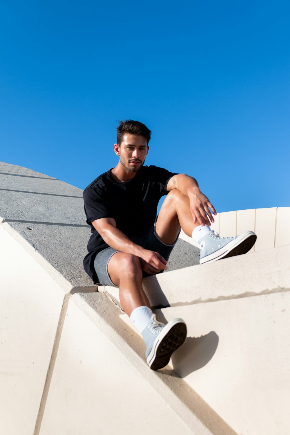 man in black crew neck t-shirt sitting on white concrete wall during daytime