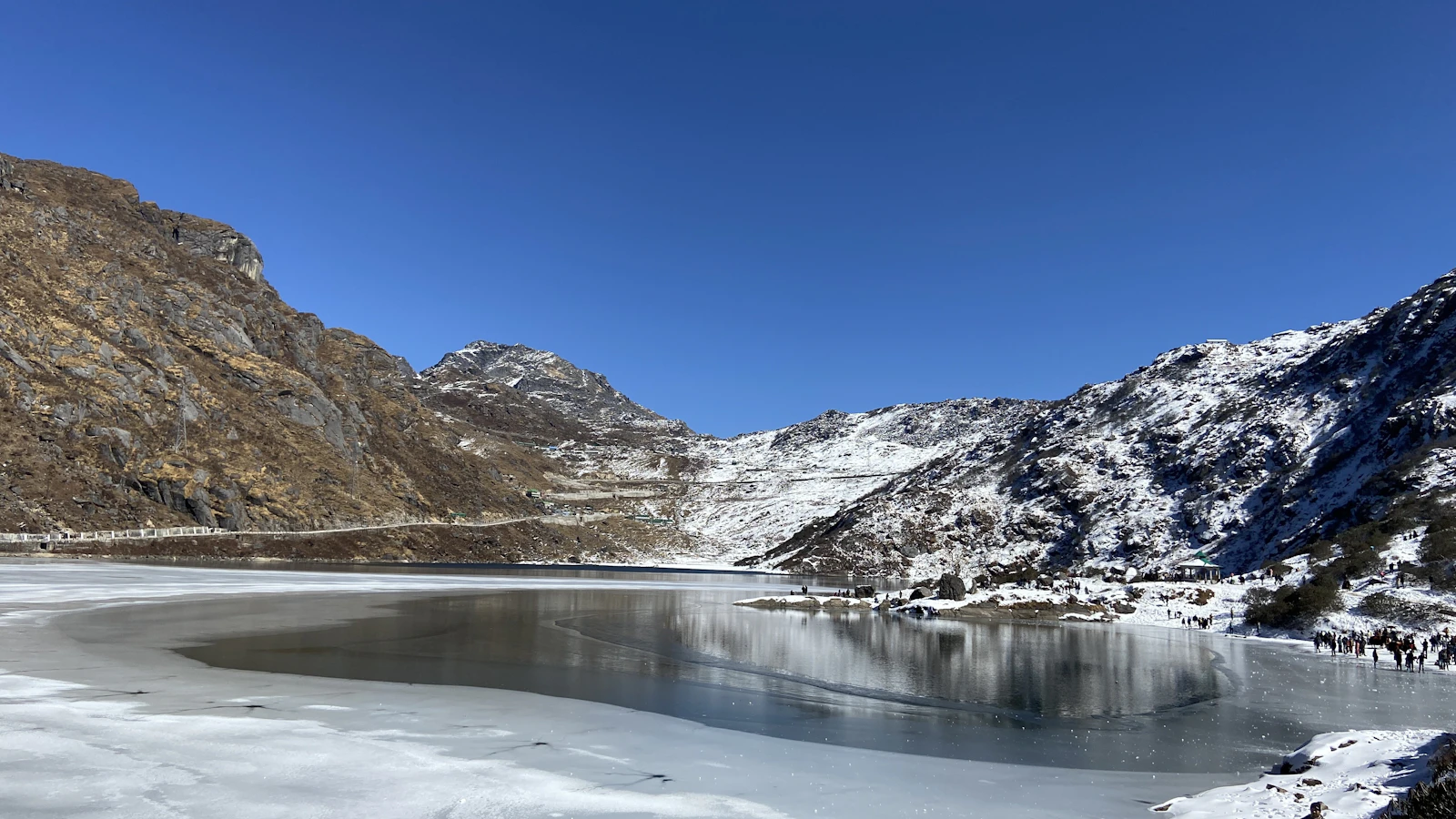 Tsomgo Lake frozen in January, snow on the brown slopes above it under a hard blue sky