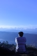 man in white shirt sitting on rock looking at mountains during daytime