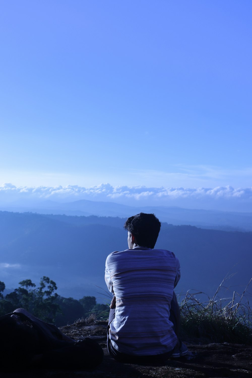 man in white shirt sitting on rock looking at mountains during daytime