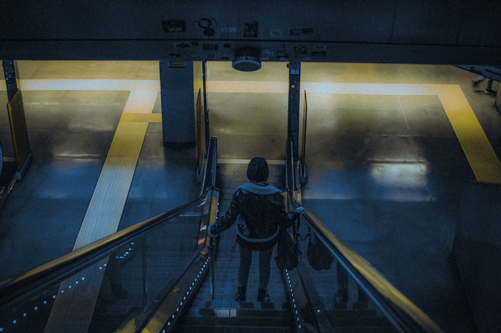man in black jacket and blue denim jeans walking on escalator