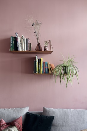 Wooden floating shelves mounted on a pink wall, filled with books and a trailing plant