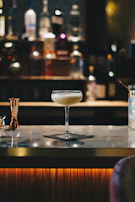 A close-up of a signature cocktail with gold flakes floating atop, set against a black marble bar.