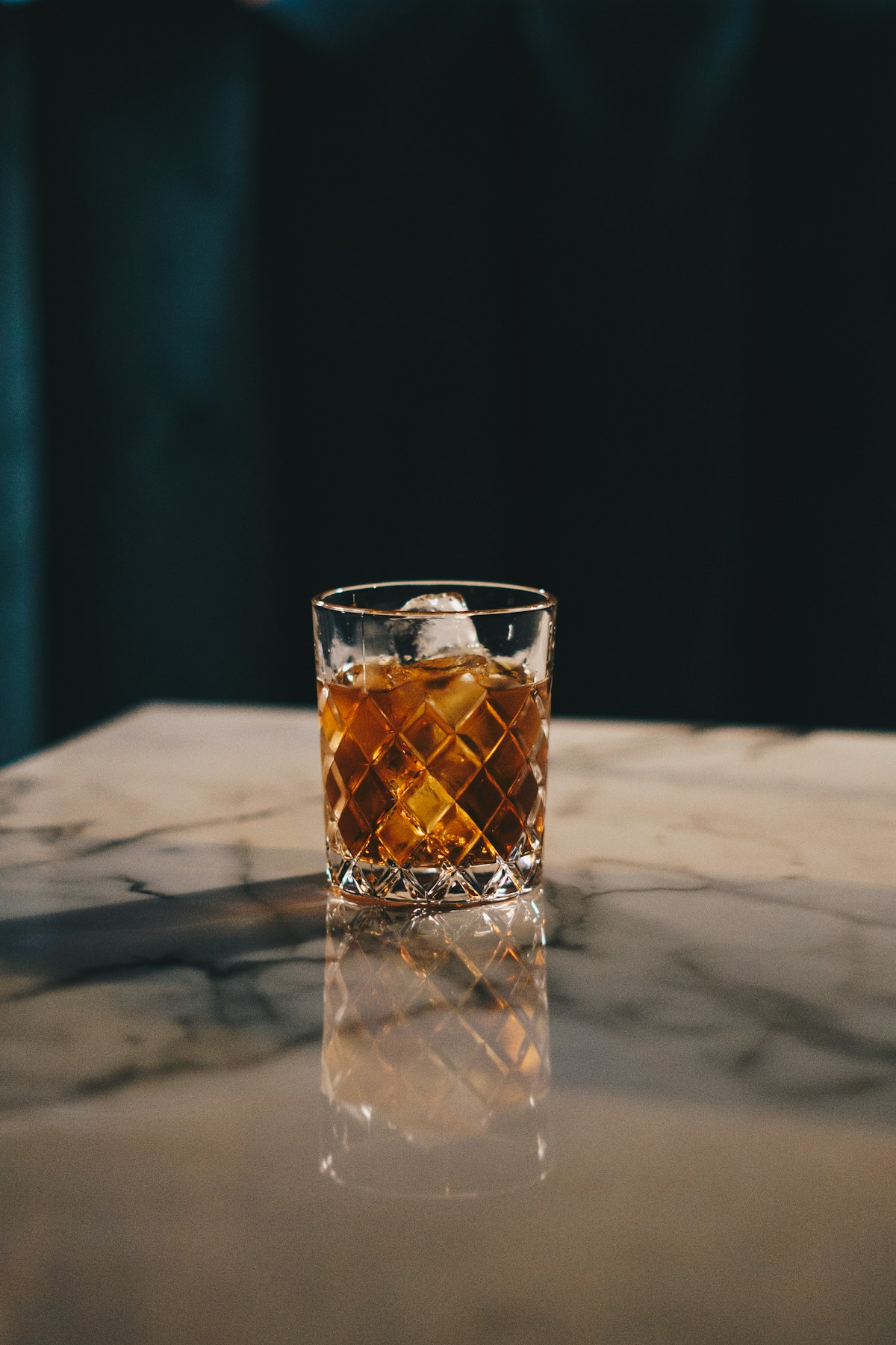 Whiskey glass with beverage and ice on granite countertop