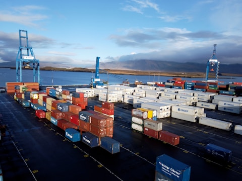 Cargo containers stacked neatly at a shipping dock with cranes in operation.