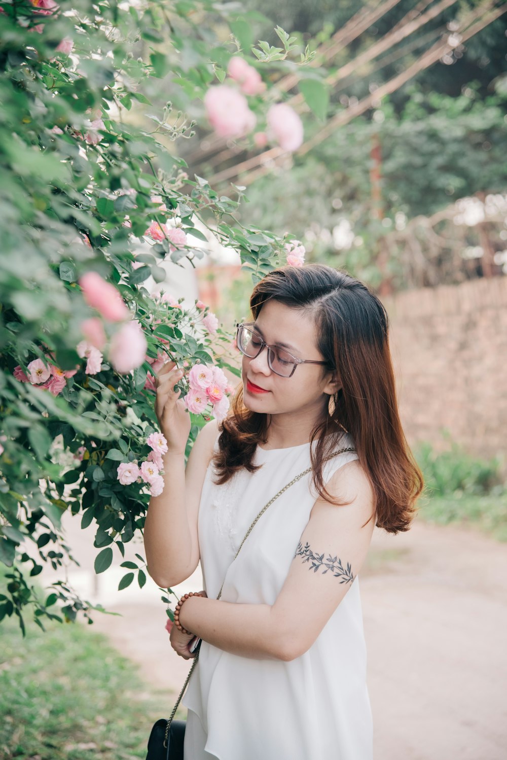 woman in white shirt wearing black framed eyeglasses standing beside green plant during daytime