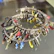 A collection of colorful keychains and small decorative trinkets attached to a circular metal band. The items include small keys, abstract shapes, and various metallic and painted charms in bright colors like red, yellow, and blue. The arrangement creates a visually striking mix of textures and forms.