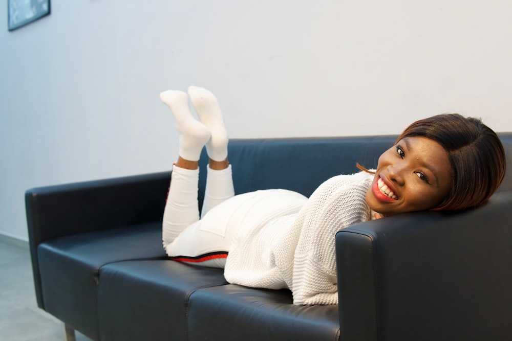 woman in white sweater lying on black couch