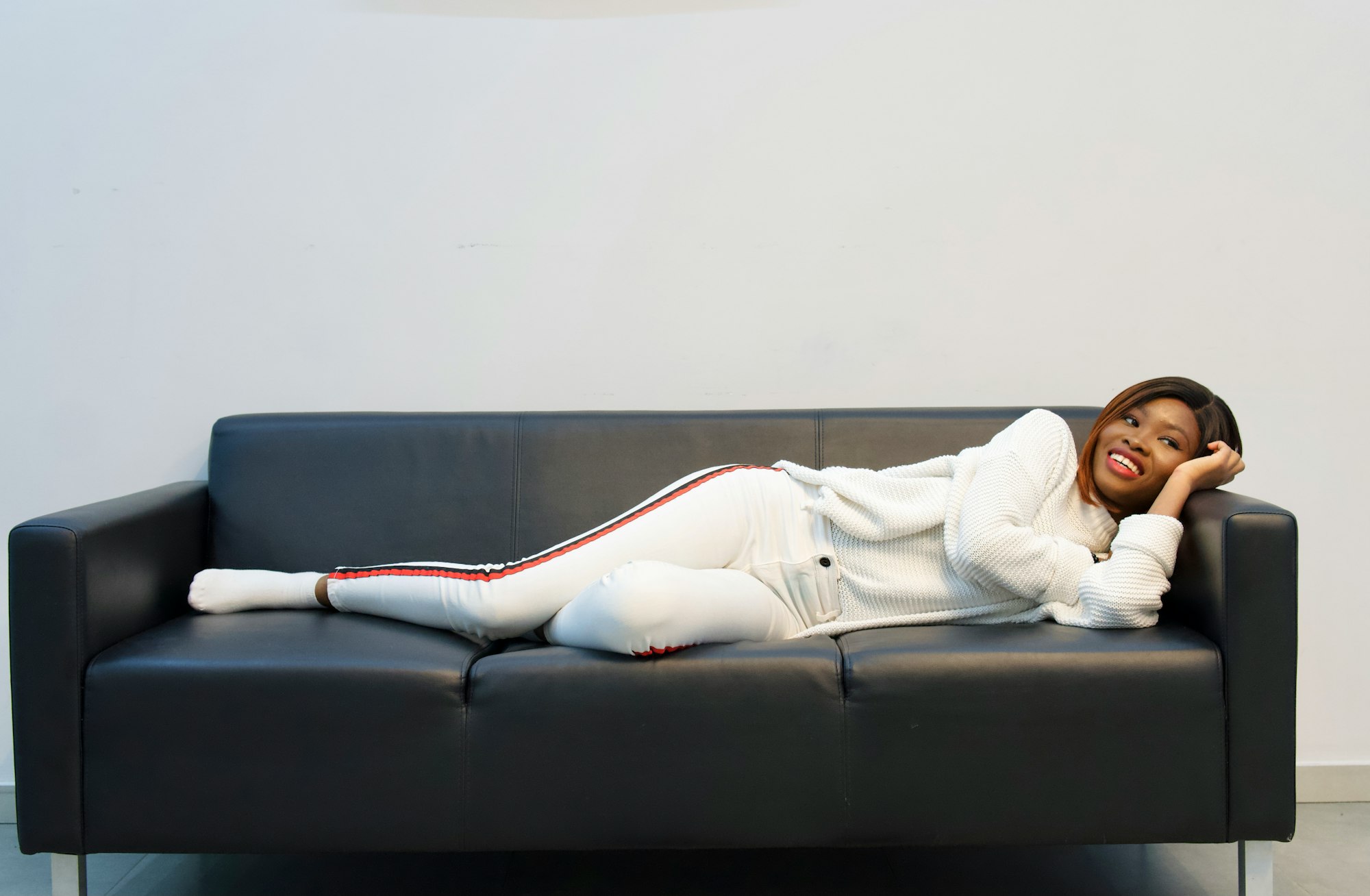 Smiling Black girl lying on a black sofa and watching tv