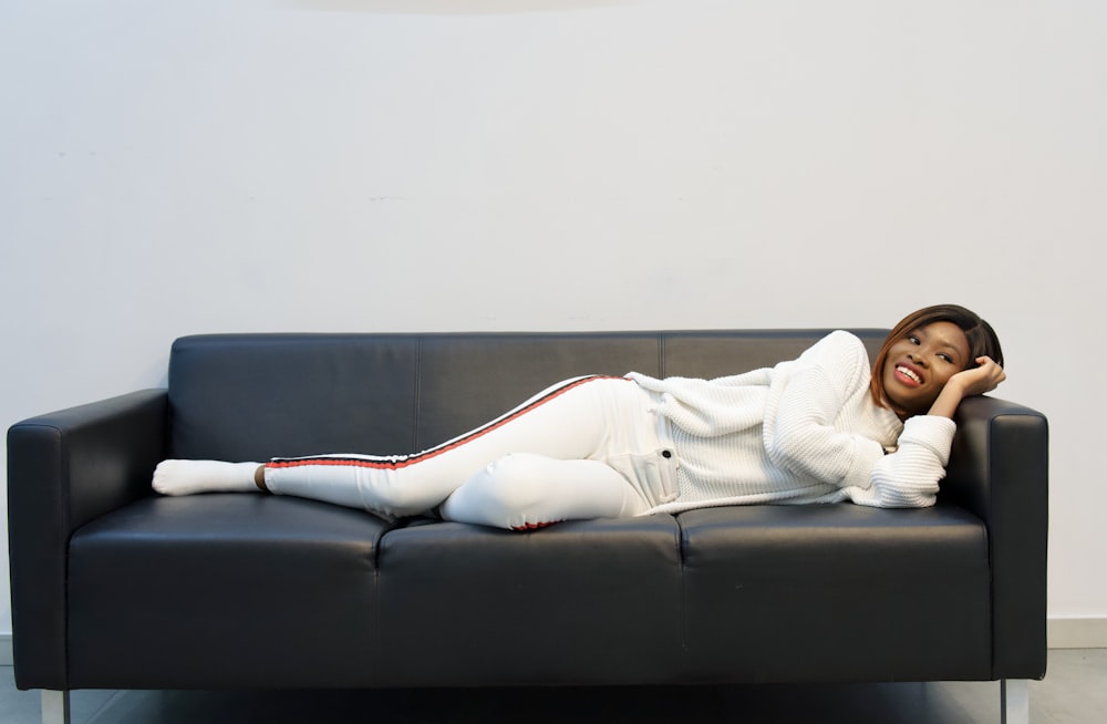 woman in white long sleeve shirt lying on black couch