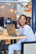 smiling woman in white dress shirt using macbook
