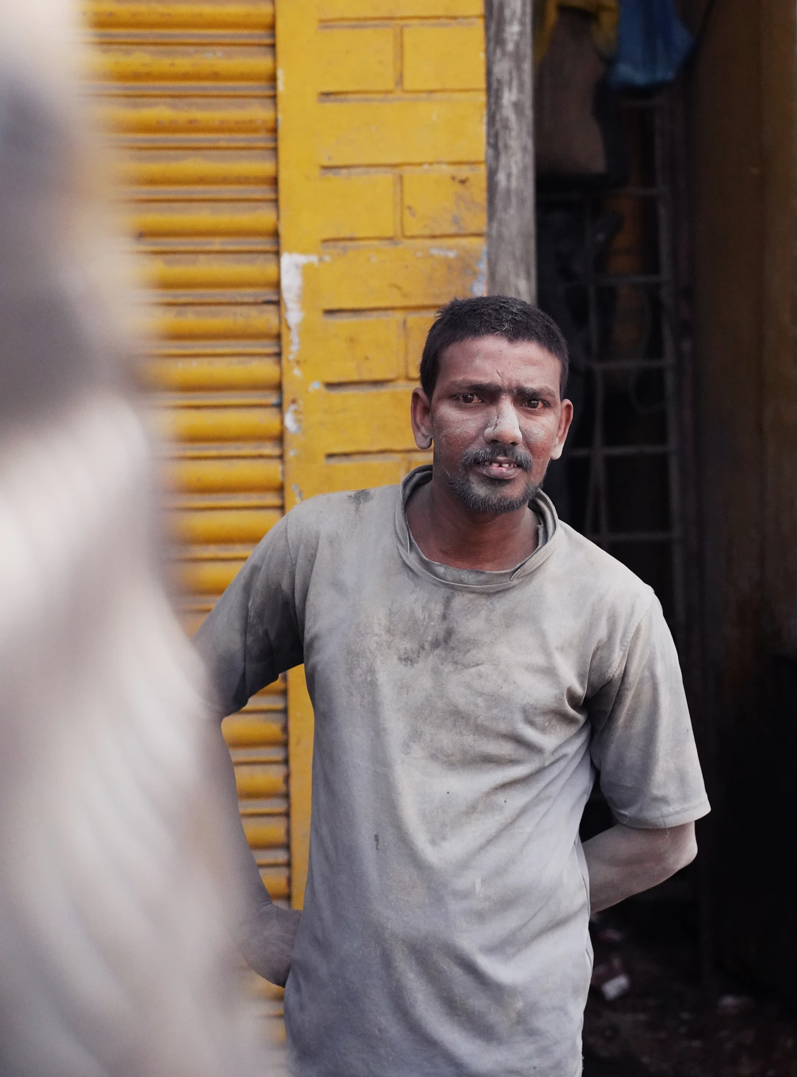 A man in a grey t-shirt standing near a wooden door