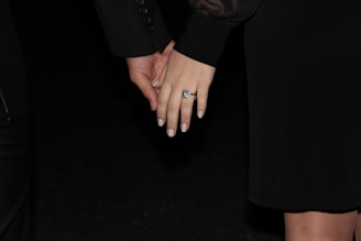 Close-up of a groom's hands holding a wedding ring against a dark, moody background.
