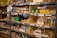 Shelves stacked with various food items including canned goods, pasta, boxed products, and bags of grains. Labels on the shelves indicate different categories of goods.