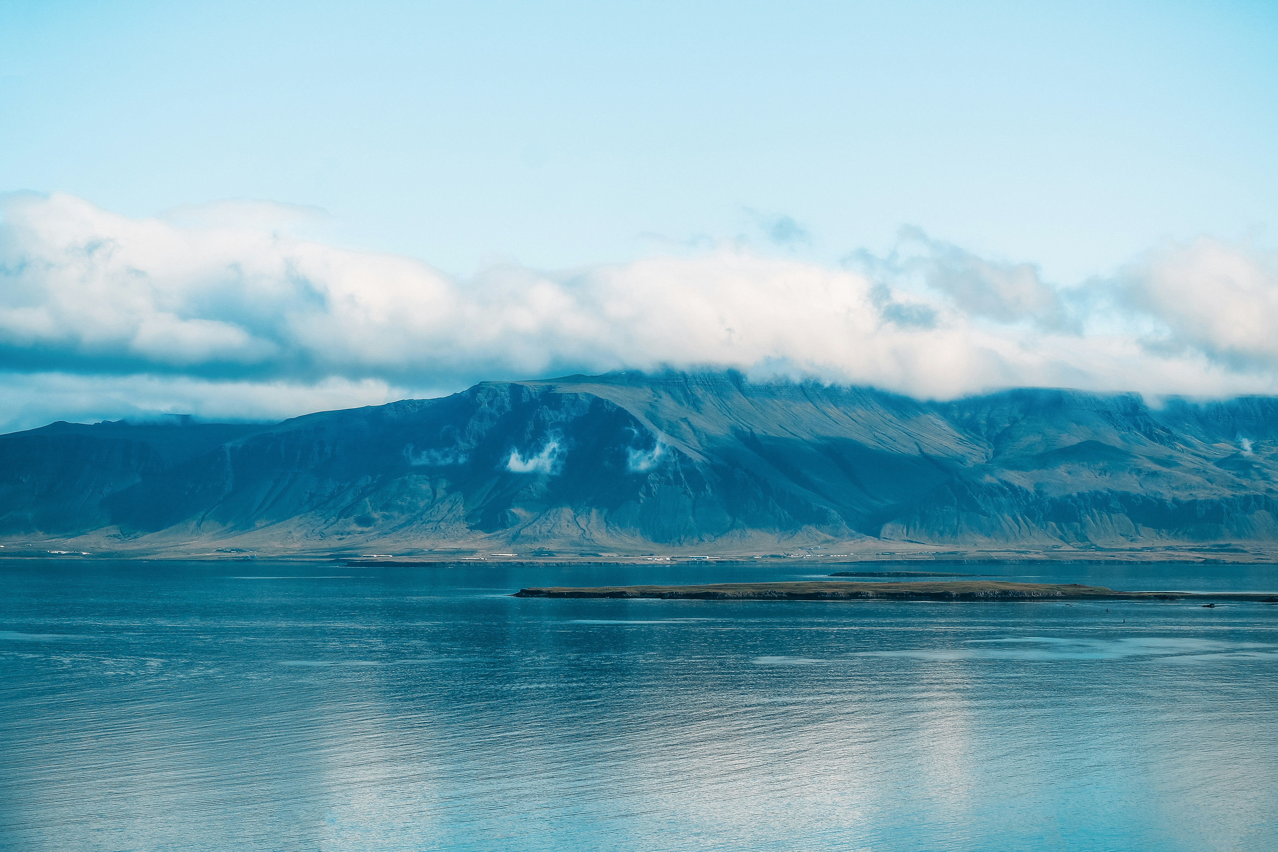 blue body of water near mountain under white clouds during daytime