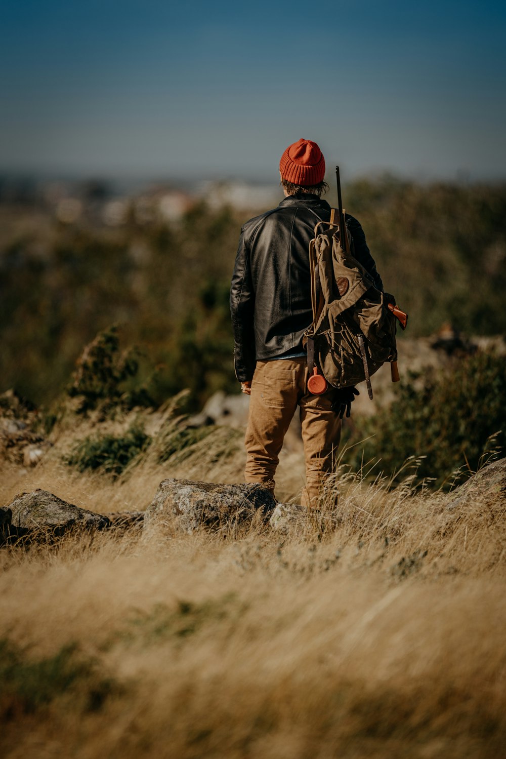 Mann in schwarzer Jacke und brauner Hose mit roter Strickmütze auf grauem Felsen stehend während