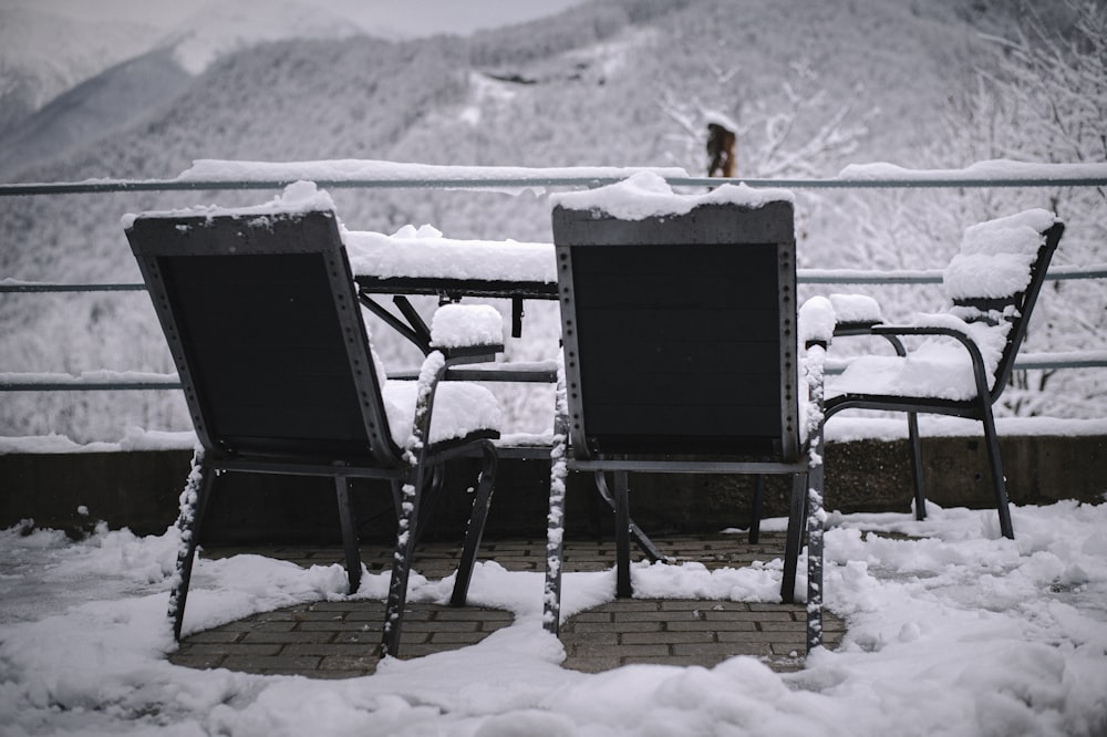2 black wooden armchairs on snow covered ground during daytime