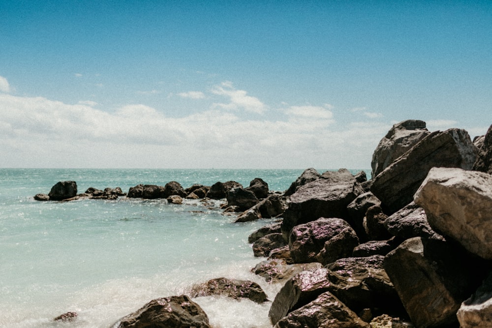 rocky shore with rocks and ocean water under blue sky during daytime