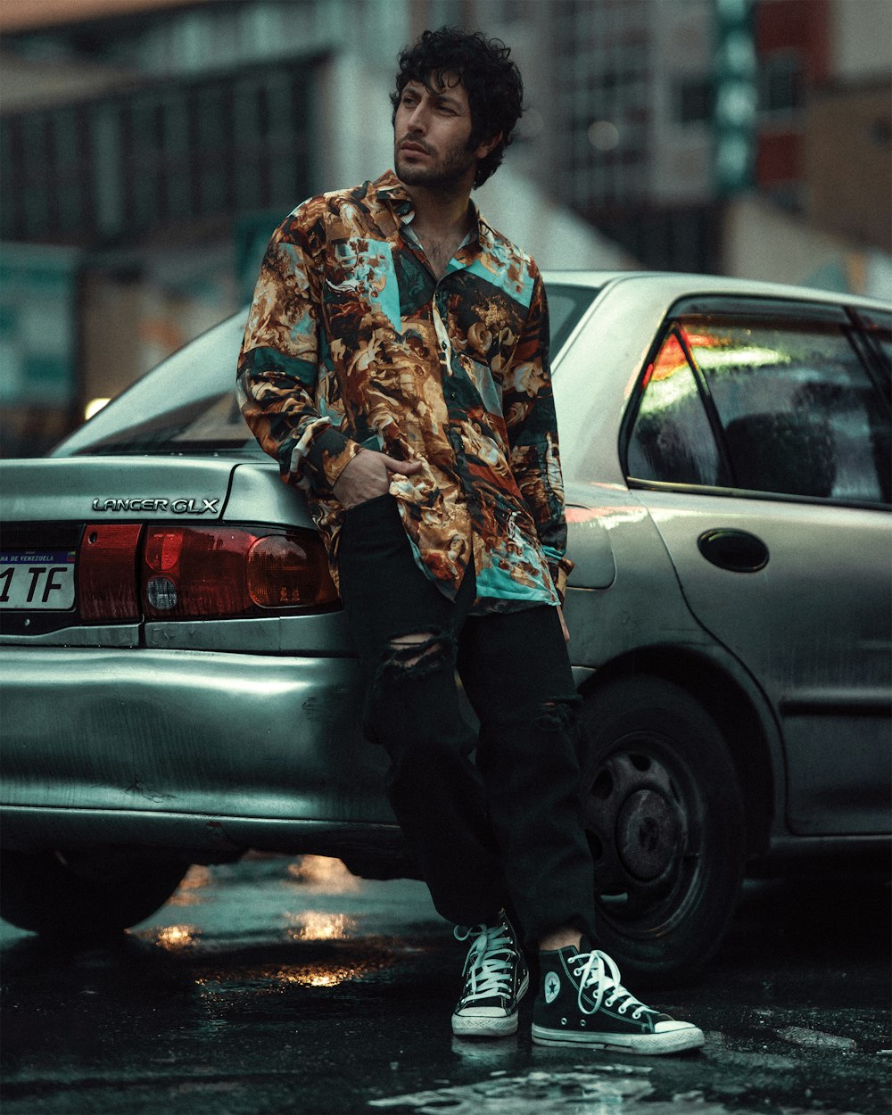 man in brown and white floral button up shirt standing beside silver sedan during daytime