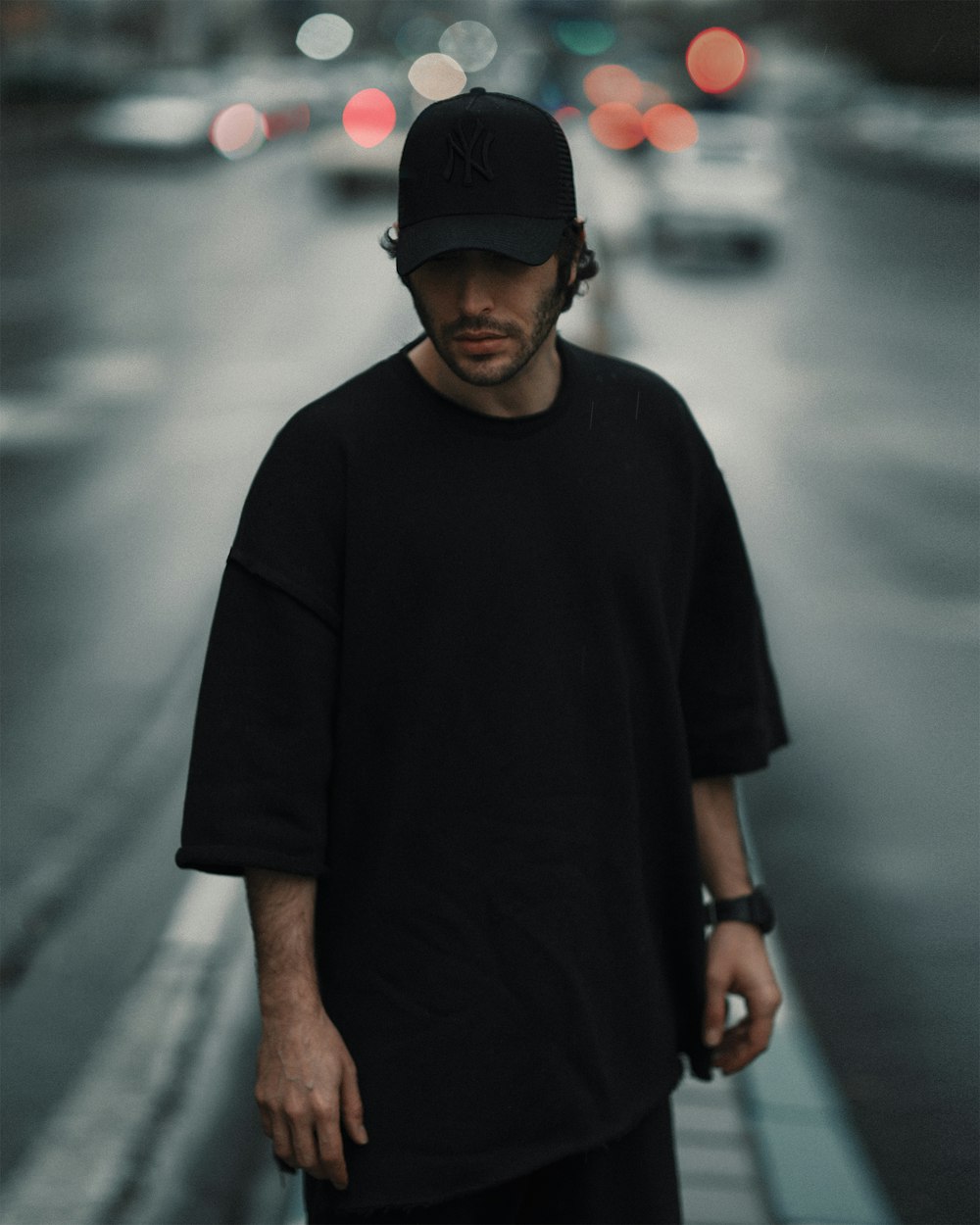man in black crew neck t-shirt and black fitted cap standing on gray concrete pavement