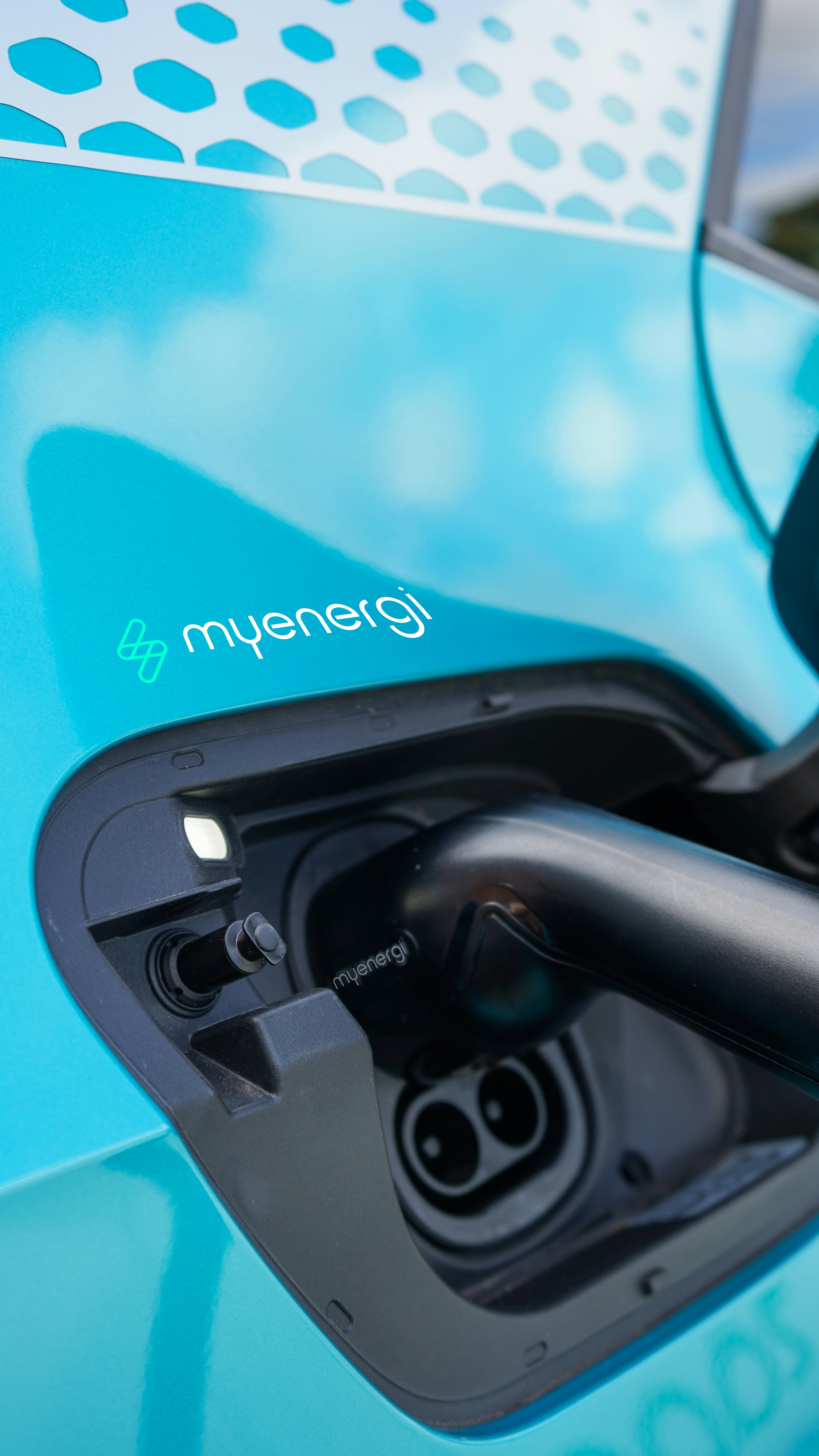 Electric vehicle charging port close-up, green charging cable plugged in, representing EV charging infrastructure