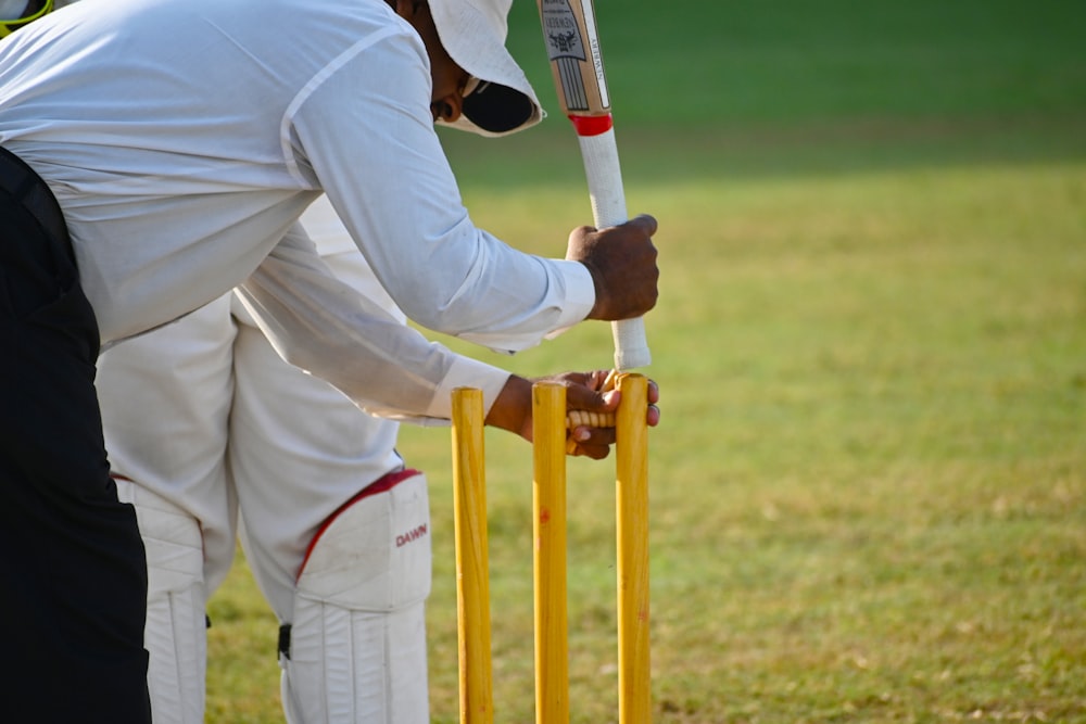 man in white pants and white shirt holding white and orange baseball bat