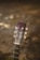 The image features the headstock of an acoustic guitar with visible tuning pegs and strings, set against a blurred earthy background. The wood of the guitar appears worn, adding a sense of vintage character.