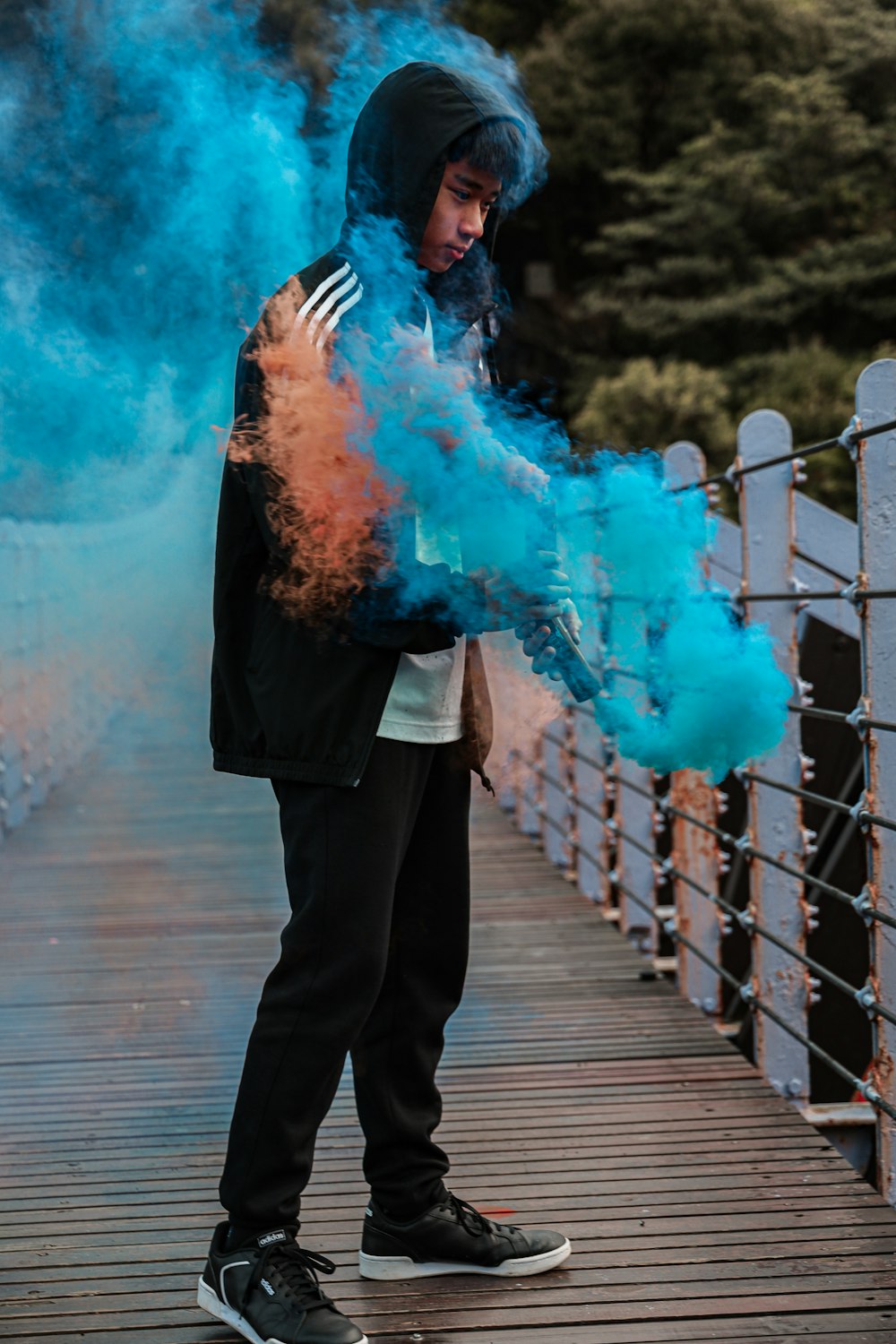 woman in black coat and pants standing on wooden bridge with blue smoke