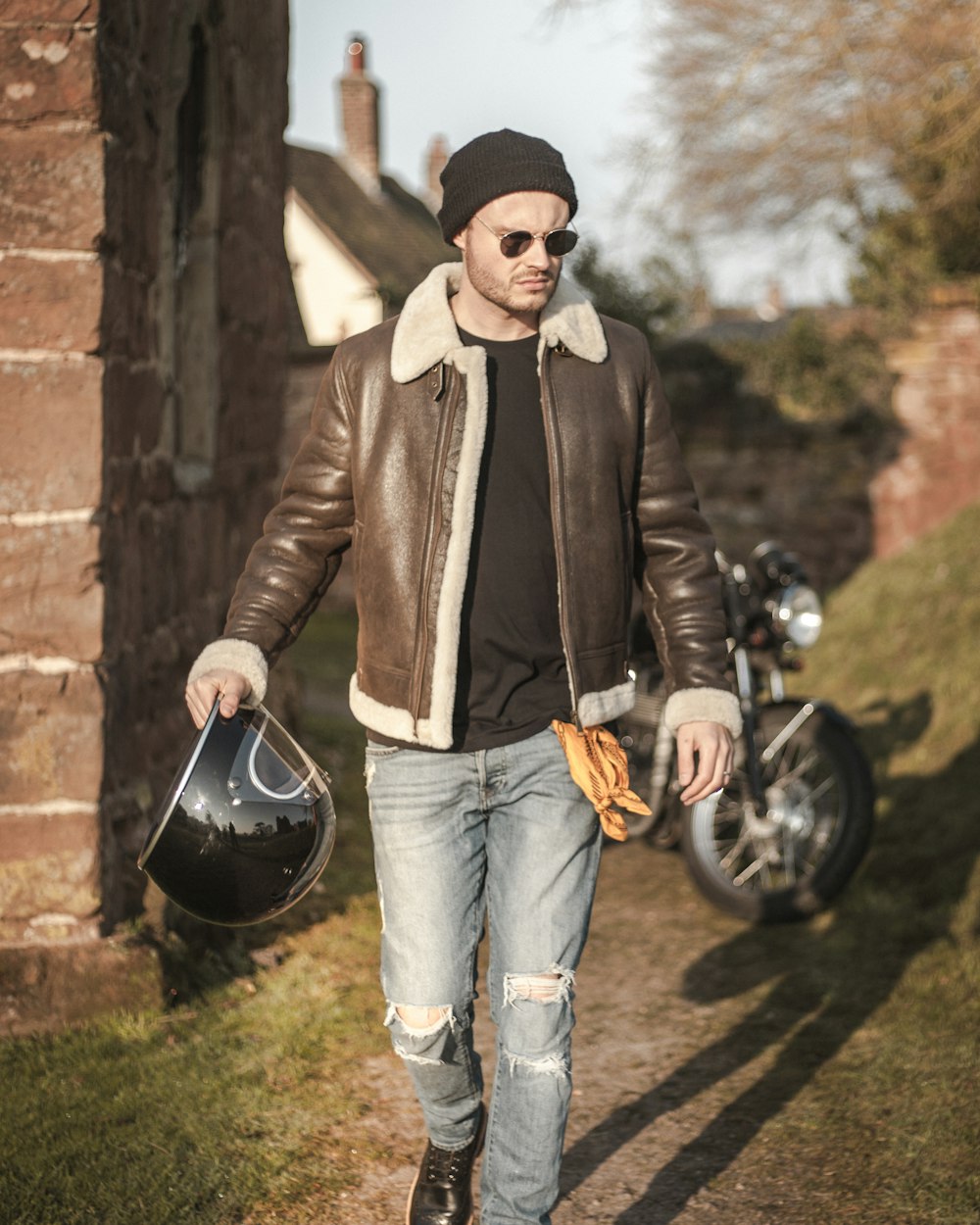 man in black leather jacket and blue denim jeans standing beside black kettle grill during daytime