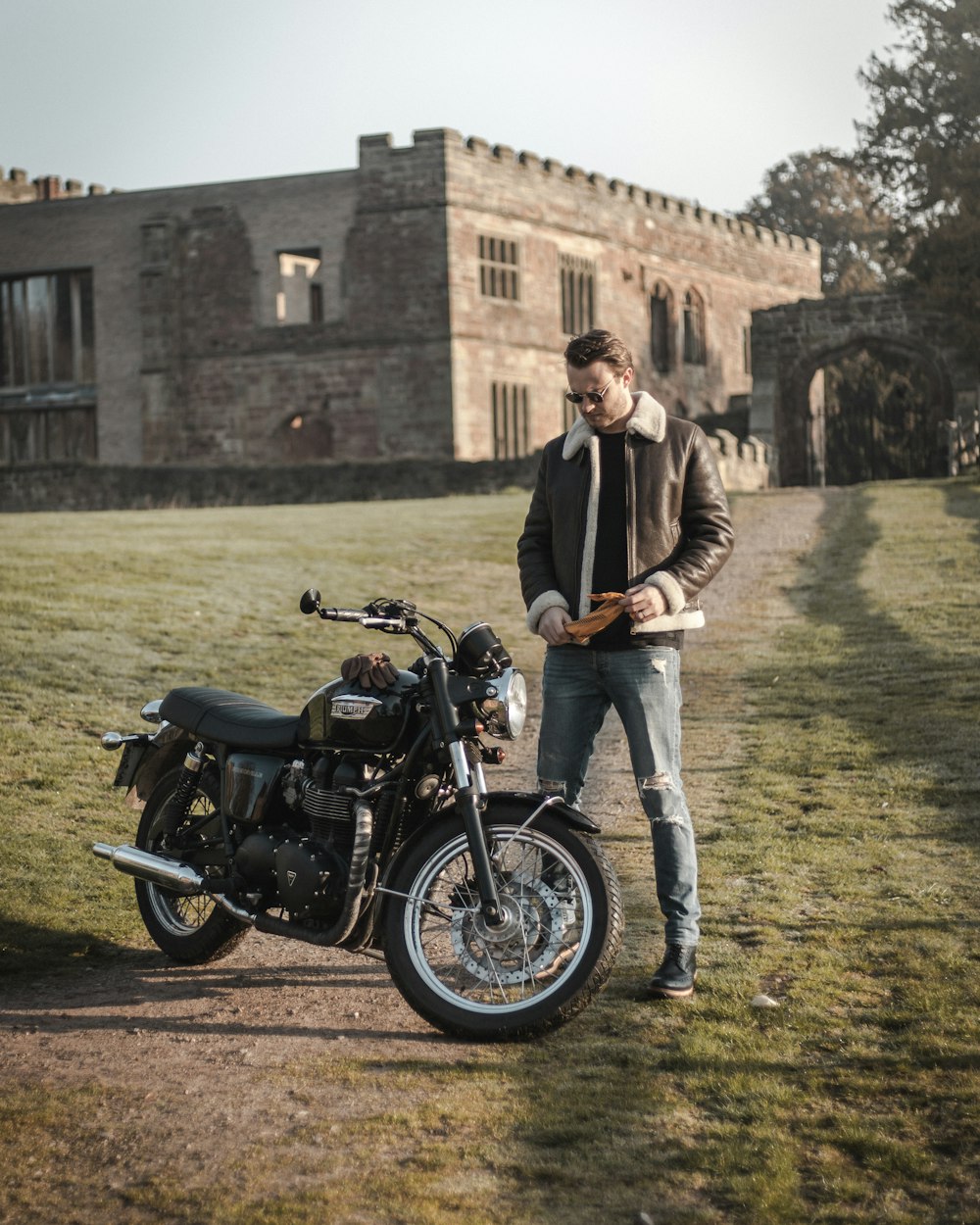 man in black jacket and blue denim jeans standing beside black motorcycle during daytime