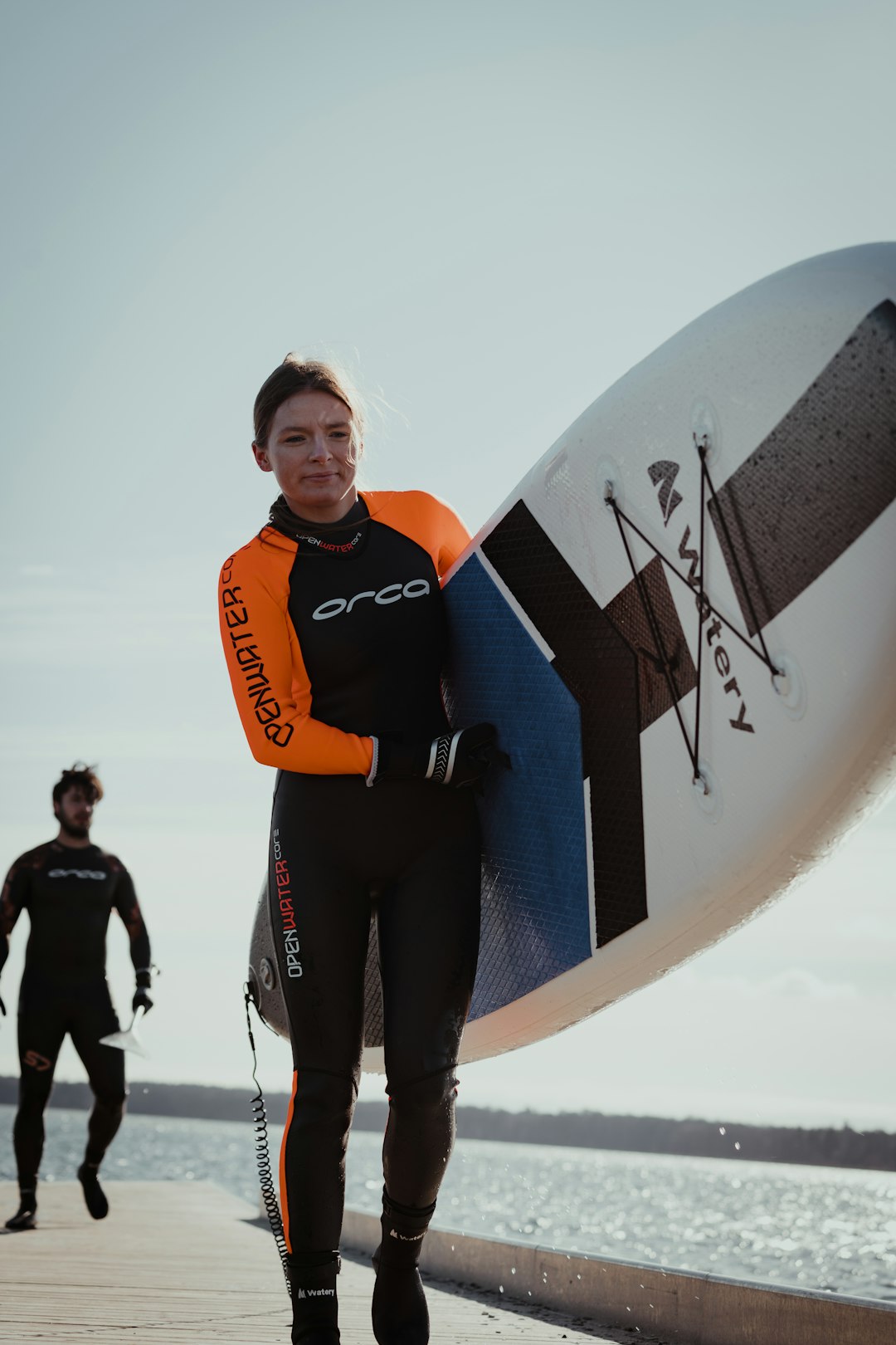 woman in orange and black jacket holding white surfboard