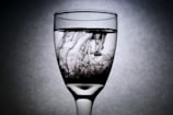 A clear wine glass filled with water showcases dark ink swirling inside, creating intricate patterns due to its flow and diffusion.