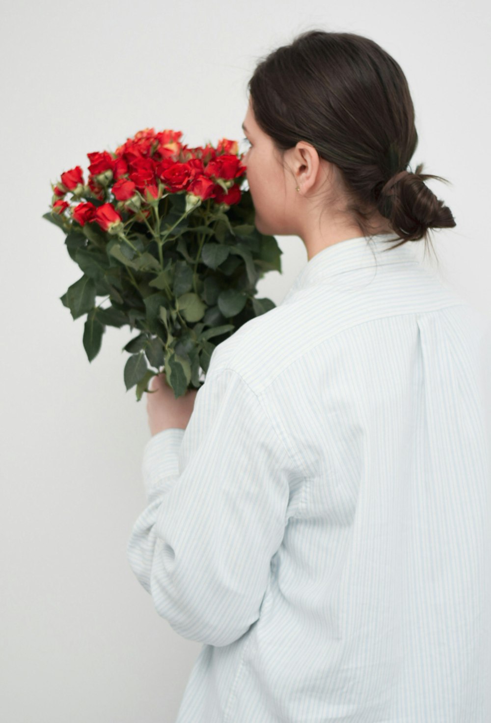 Frau im weißen Langarmhemd mit rotem Rosenstrauß