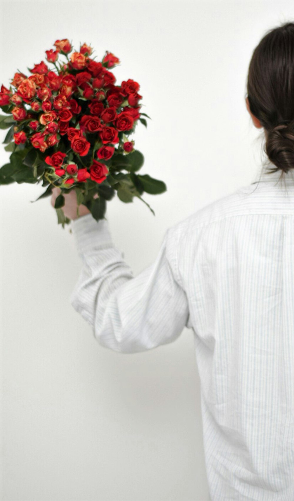 Femme en chemise blanche à manches longues tenant un bouquet de roses rouges