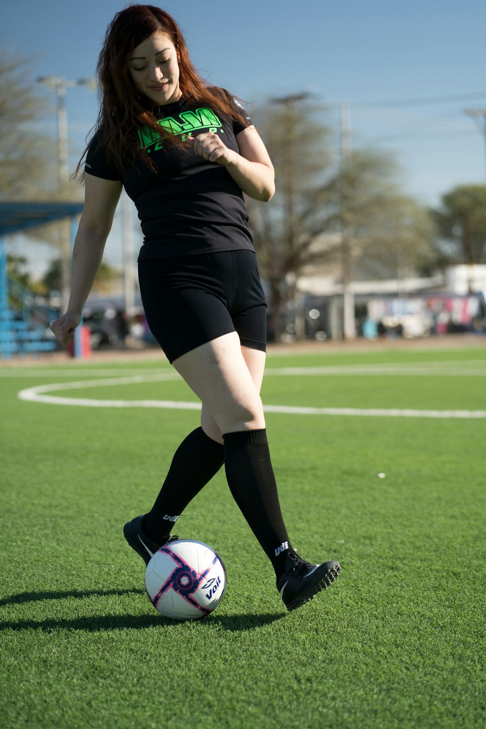 woman in black and green shirt and black shorts playing soccer during daytime