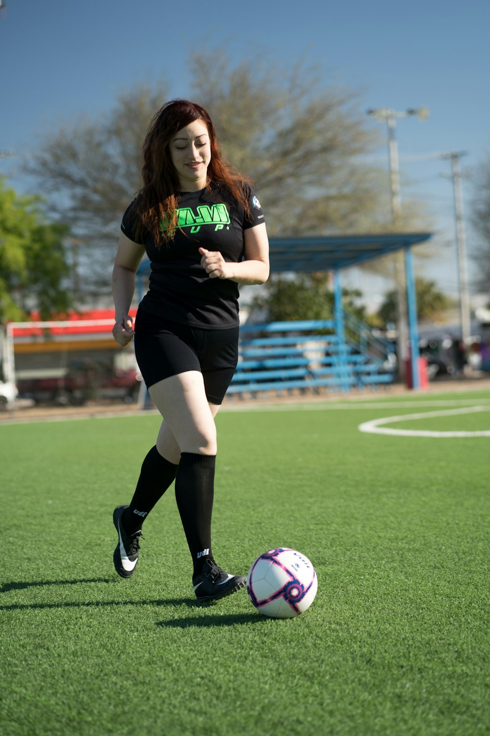 Frau im schwarz-grünen Nike-Fußballtrikot kickt Fußball auf grünem Rasenplatz während