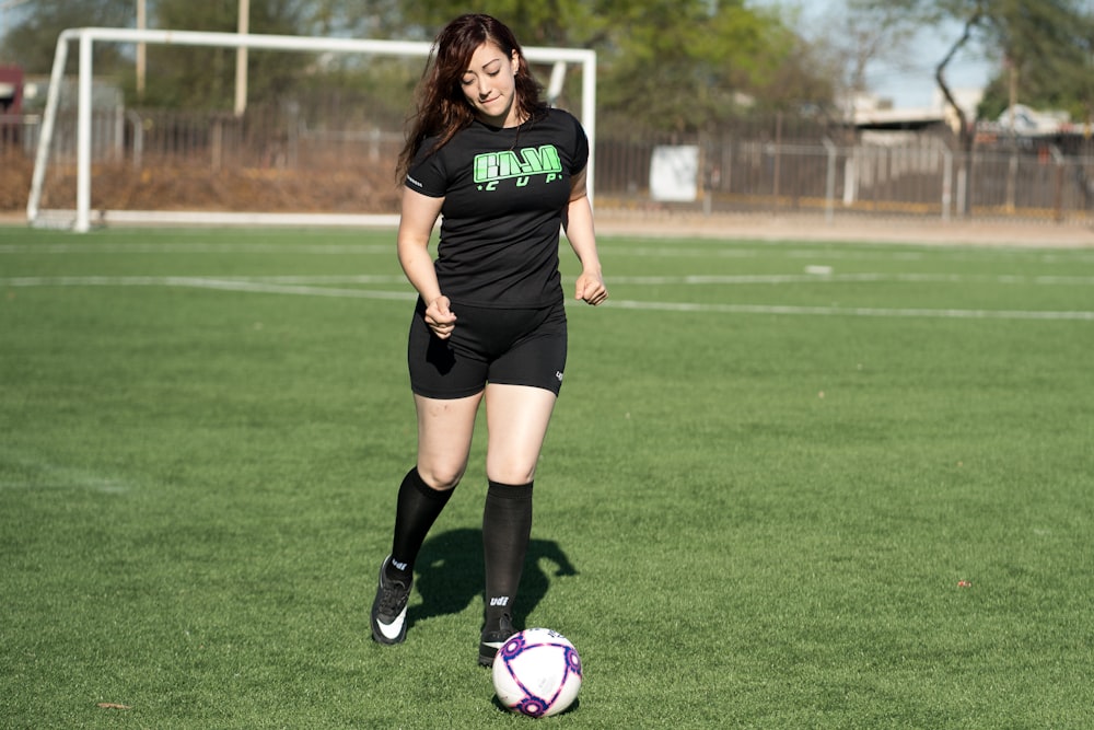 woman in black nike soccer jersey kicking soccer ball on green grass field during daytime