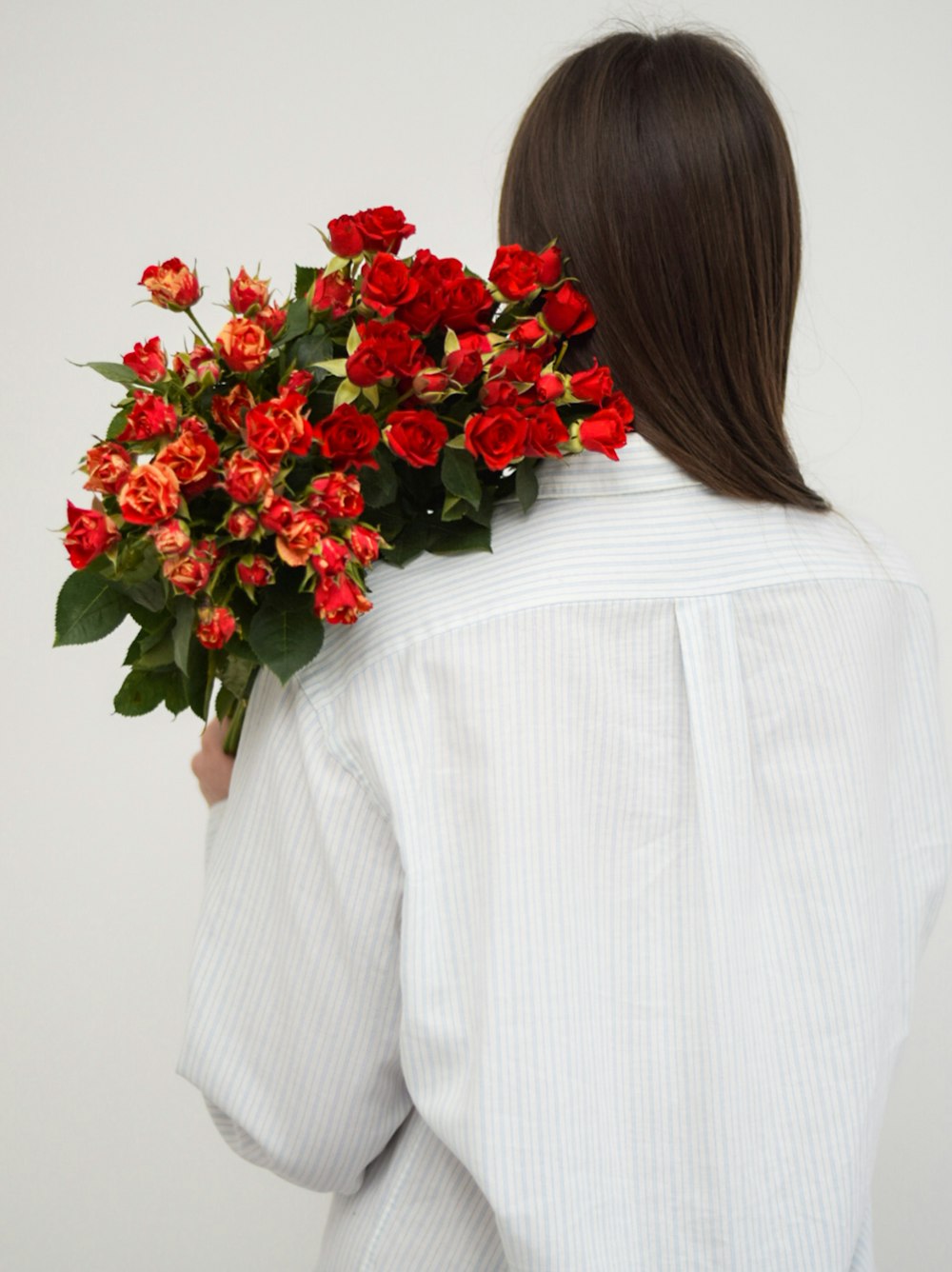 Mujer en camisa blanca de manga larga sosteniendo ramo de rosas rojas