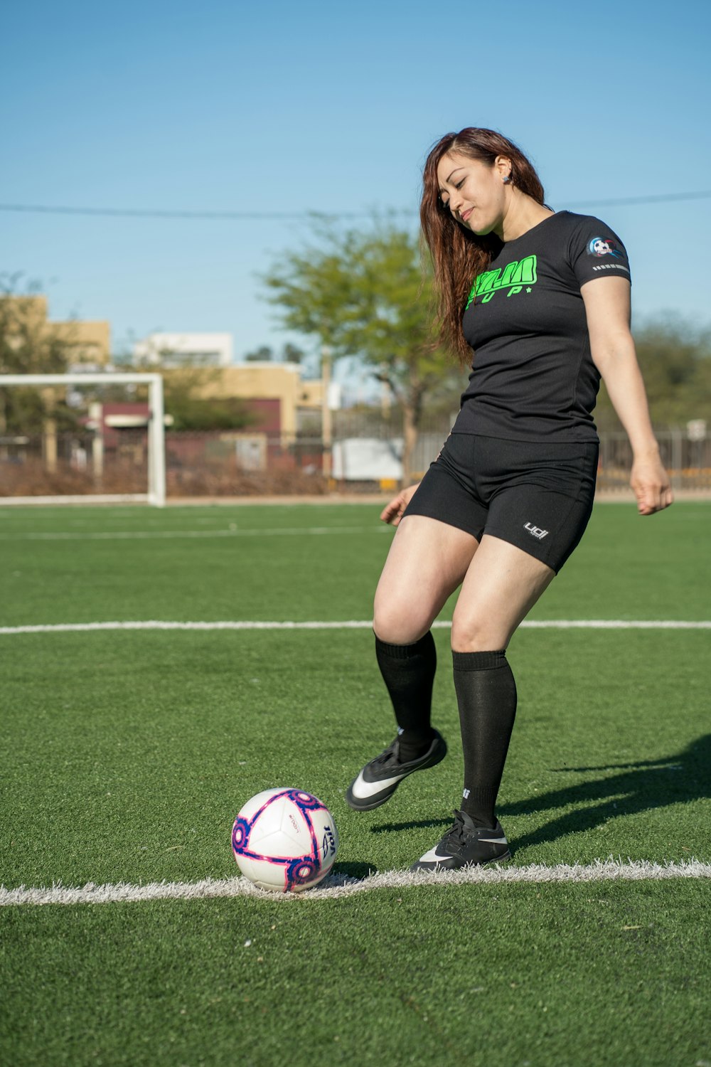 woman in black and white nike soccer jersey kicking soccer ball on green grass field during