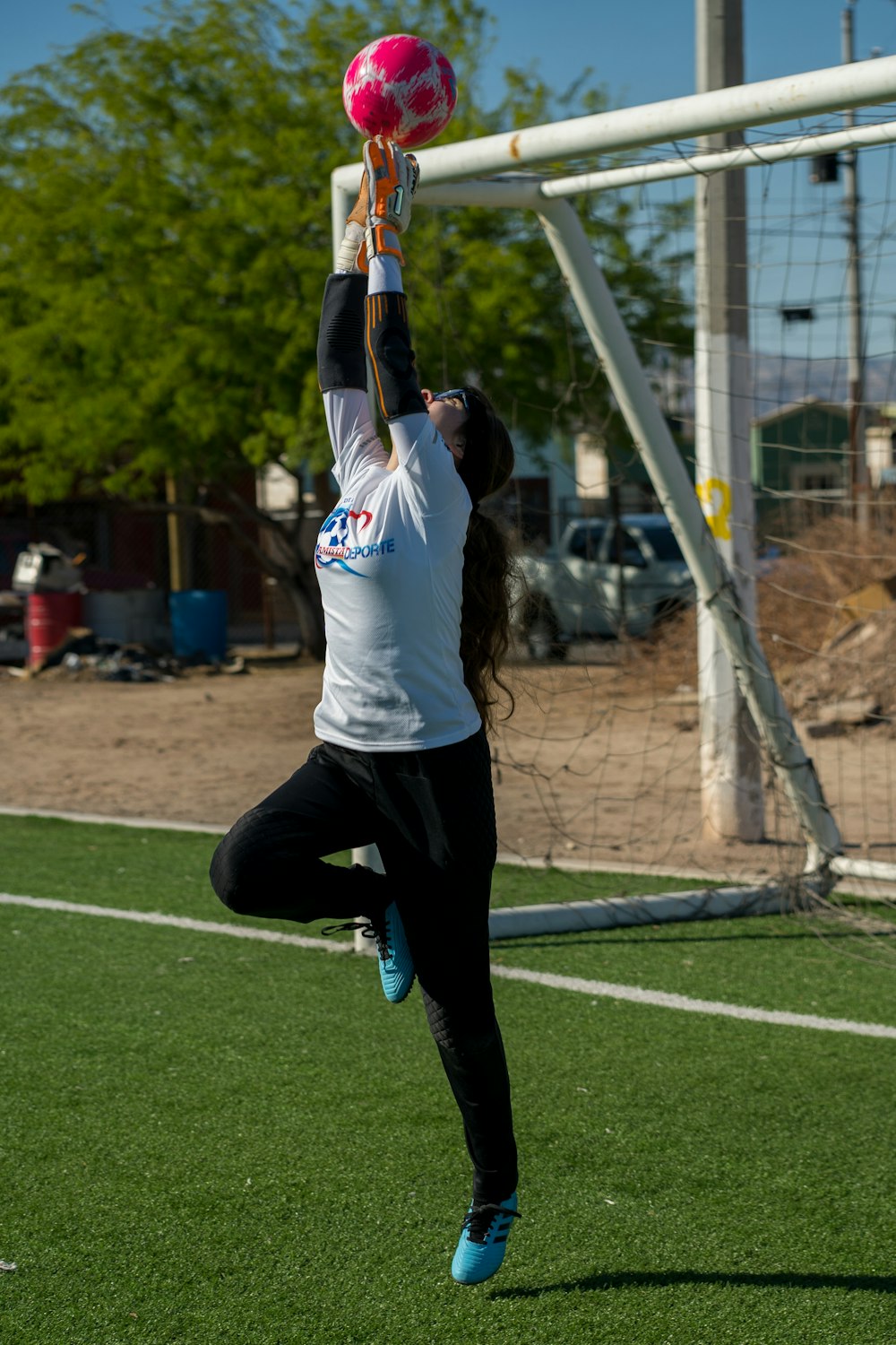 woman in white and red crew neck t-shirt and black pants jumping on green field