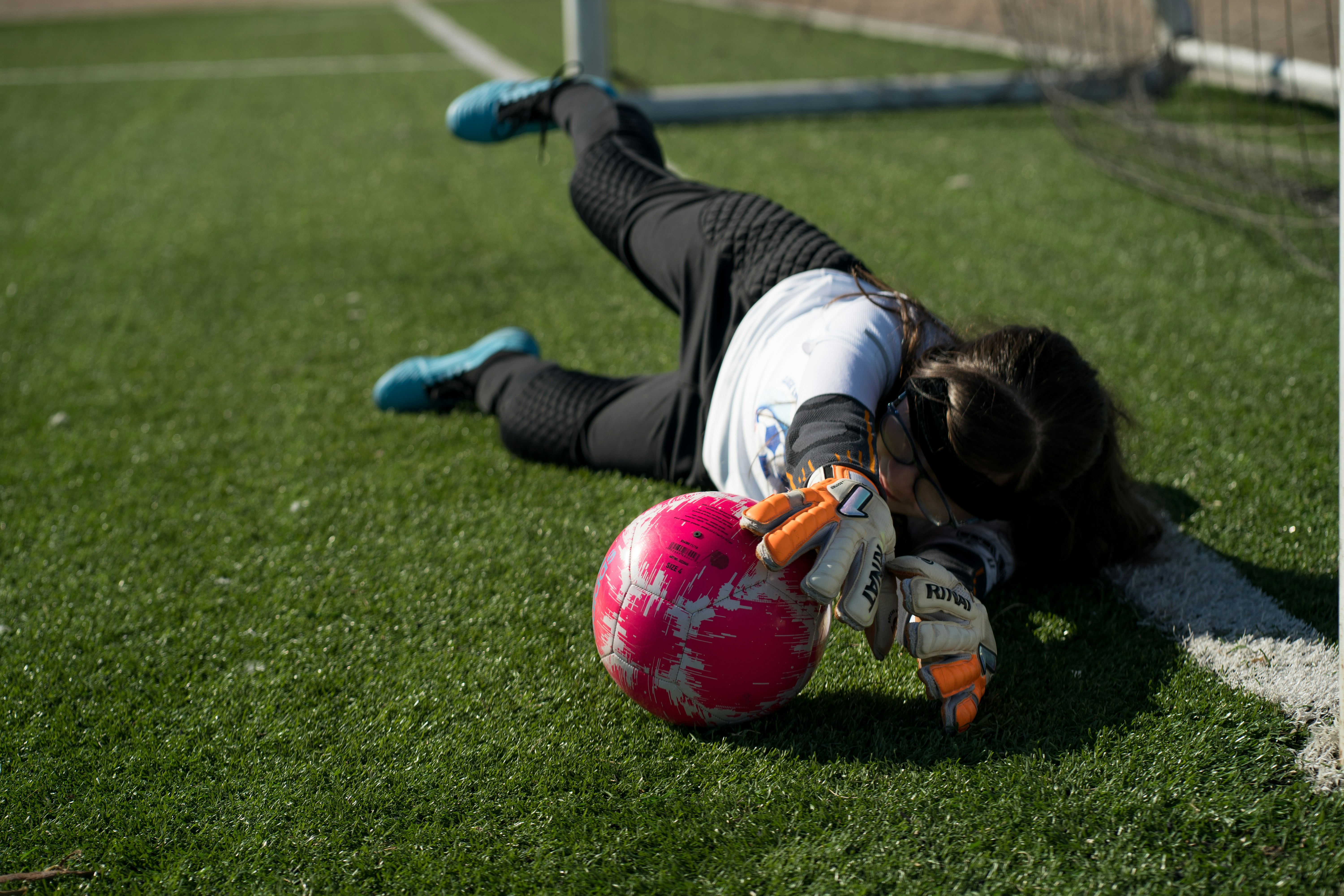 woman in white long sleeve shirt and black pants playing soccer on green grass field during