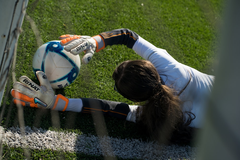 girl in white long sleeve shirt playing soccer on field during daytime