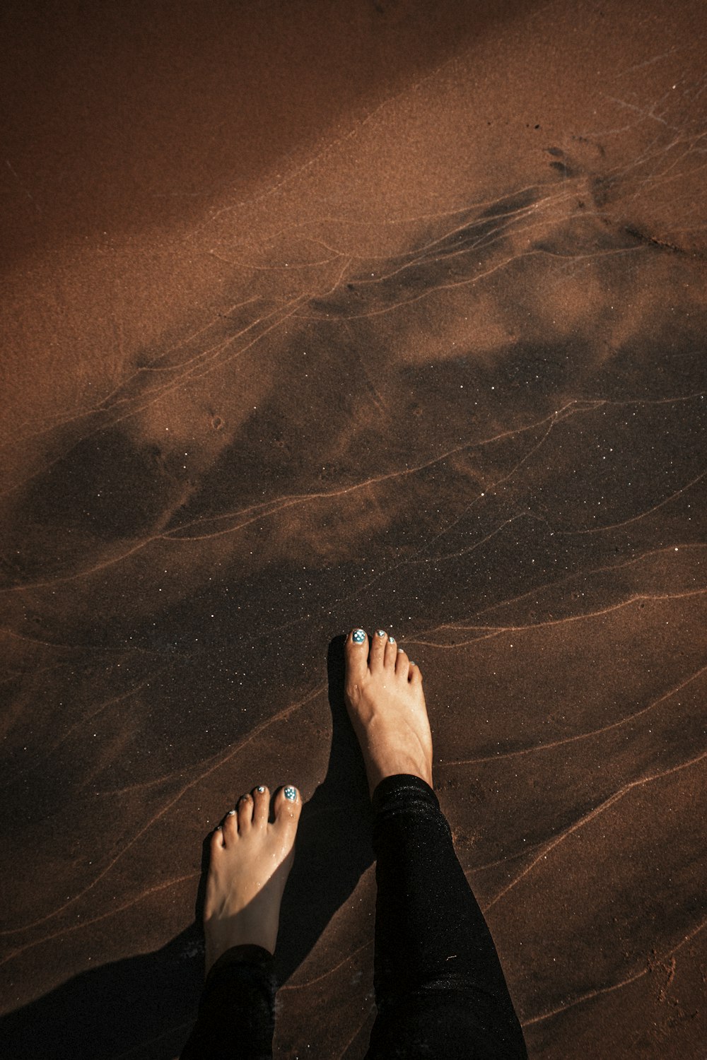 person in black pants standing on brown sand