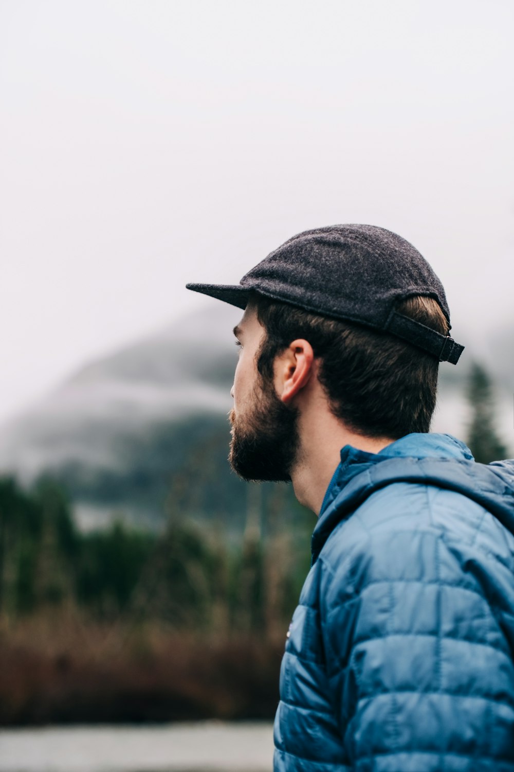 Mann in blauer Jeansjacke und schwarzer Mütze mit Blick auf den Berg tagsüber