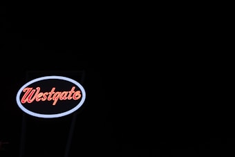 A neon sign displaying the word 'Westgate' is illuminated against a dark, black background. The sign features red lettering encased in an oval with a white border, creating a striking contrast with the night sky.
