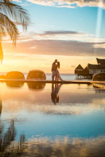 Couple embracing at sunset near overwater bungalows, reflecting honeymoon travel planning Canada cou