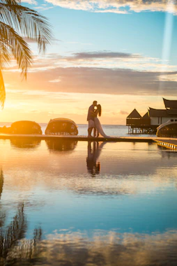 Couple embracing at sunset near overwater bungalows, reflecting honeymoon travel planning Canada cou