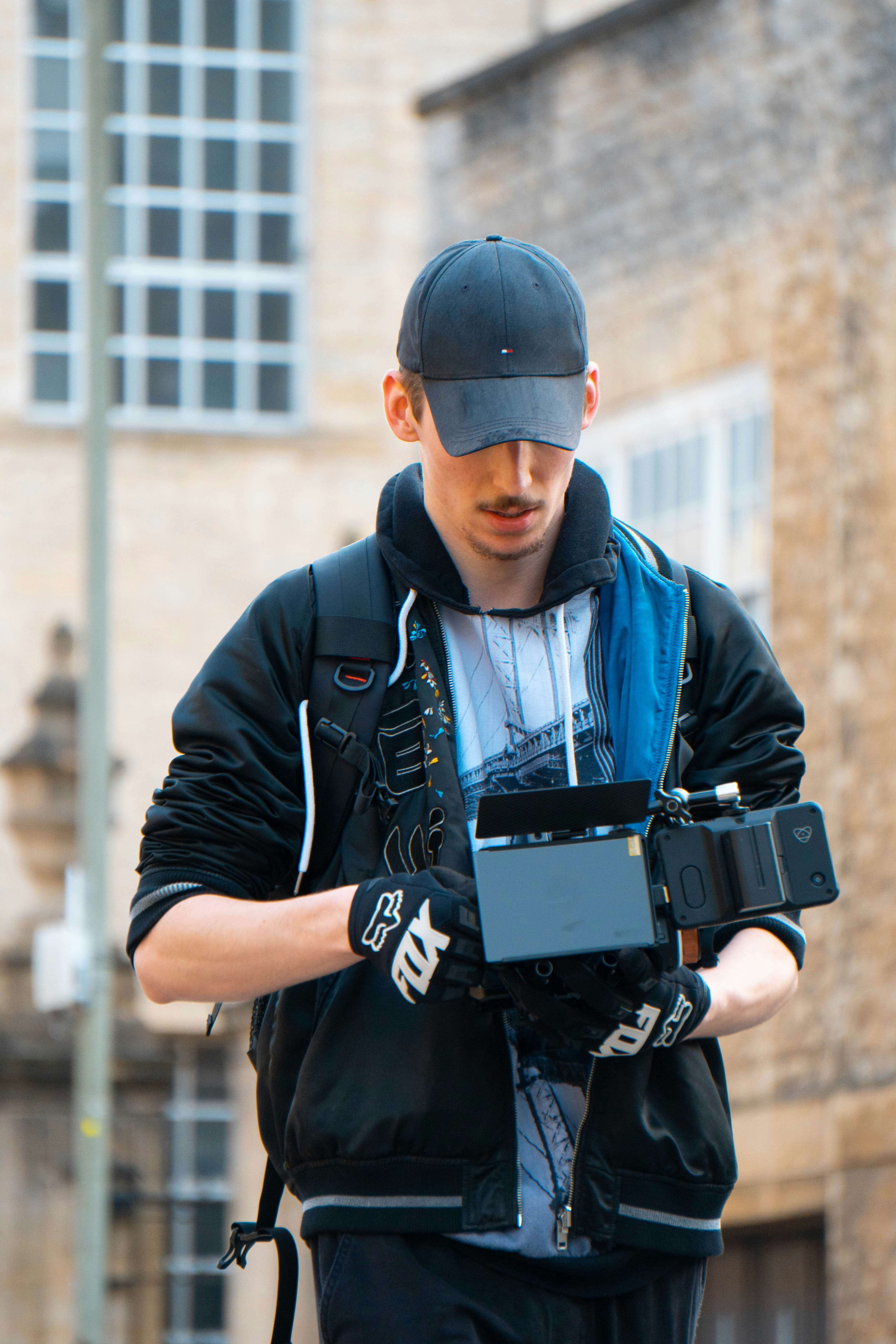 man in black jacket and blue denim jeans holding black dslr camera
