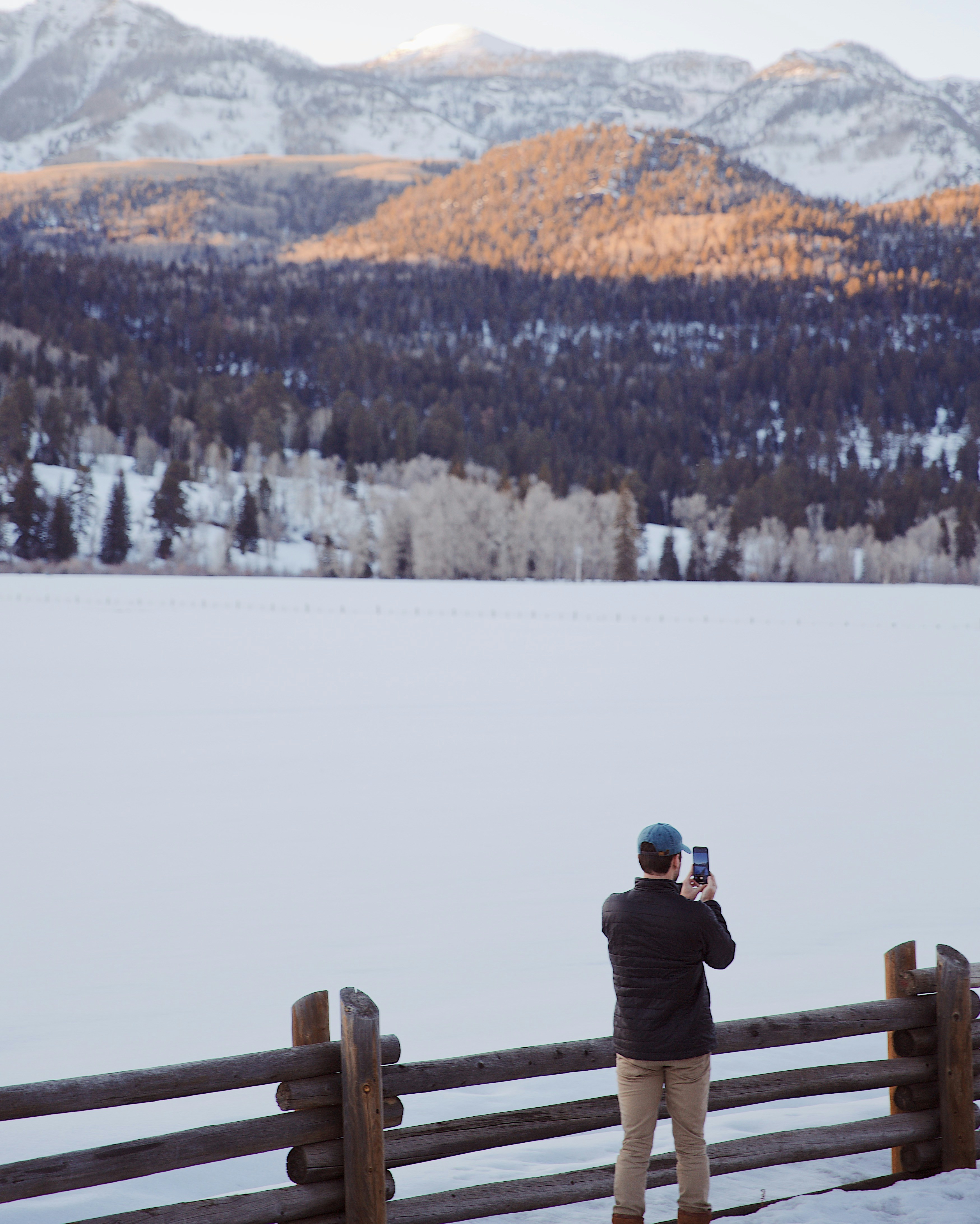 昼間、茶色の木製の柵の上に立つ黒いジャケットとブルーデニムのジーンズの男性